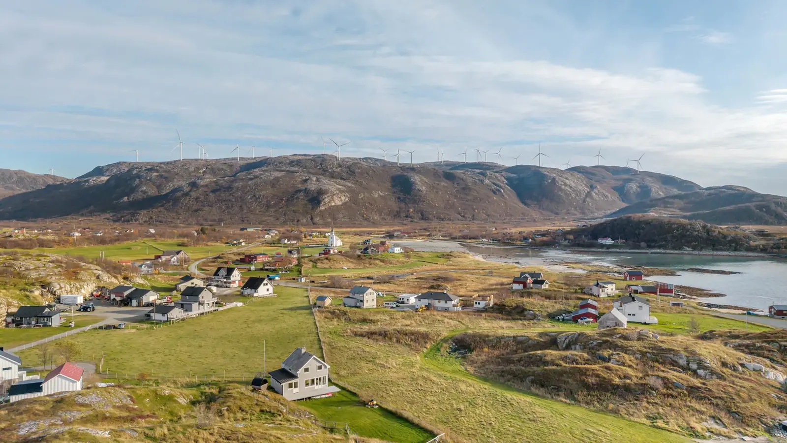 Drohnenaufnahme von Brensholmen mit weisser Kirche, Windkraftanlagen auf den Höhen und ruhiger Bucht